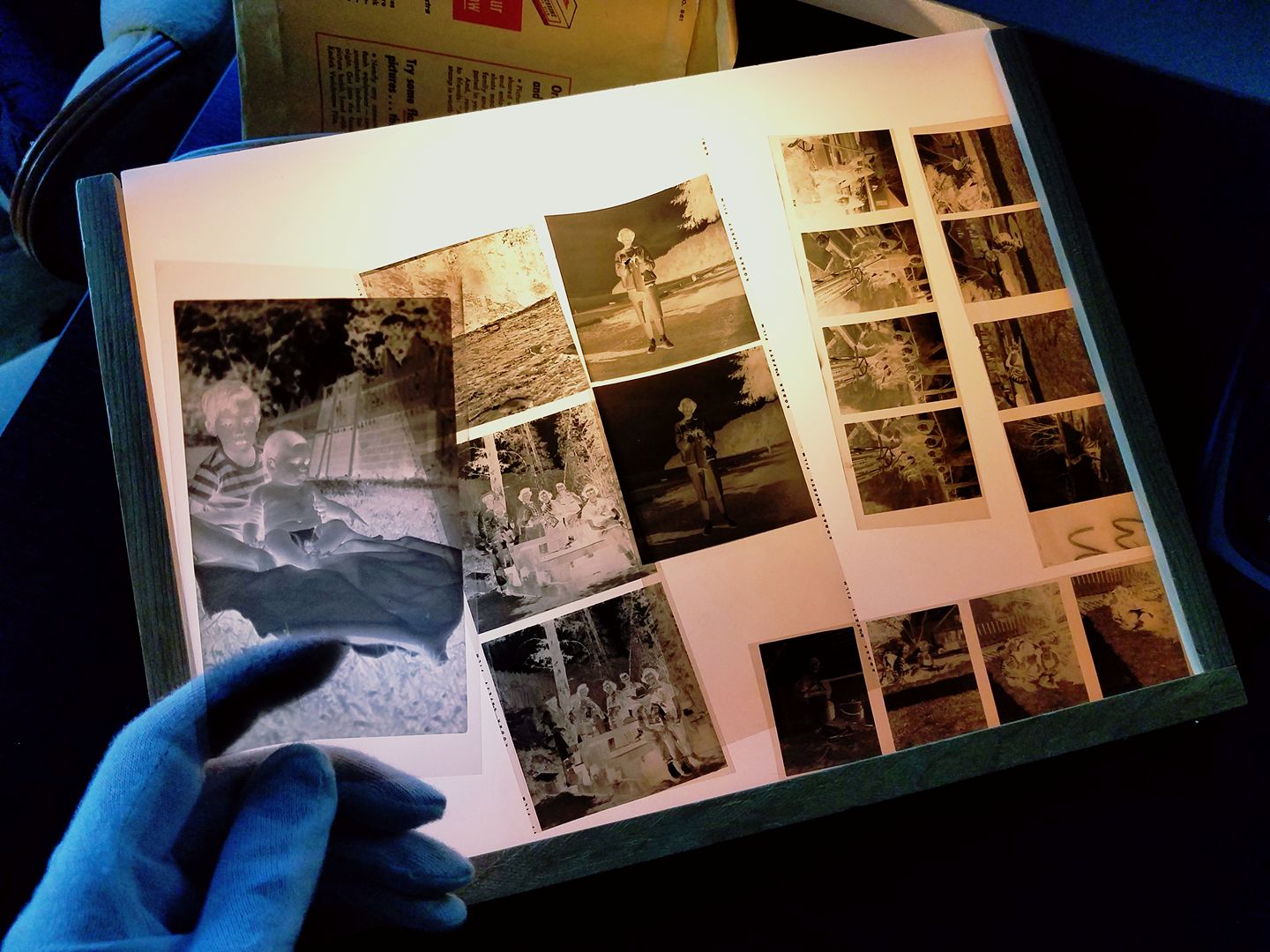 Negatives of various sizes on a light table, and one held by a hand in a white cotton glove.